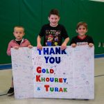 kids holding a thank you gold khourey and turak sign
